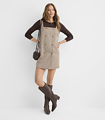 A woman in a brown long-sleeved shirt and a plaid pinafore dress with knee-high boots and a crossbody bag stands against a plain white background. carousel Product Image 2