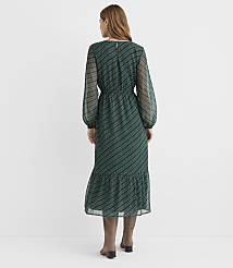A woman in a green patterned dress and brown boots stands against a plain white background. carousel Product Image 3