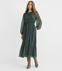 A woman in a long, green, patterned dress stands against a plain, light gray background. carousel Product Image 1