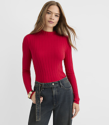 A woman in a red ribbed turtleneck and dark jeans stands against a plain white background. carousel Product Image 1