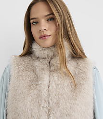 A woman with long blonde hair wears a light beige fur vest over a light blue blouse against a plain white background. carousel Product Image 4