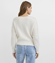A woman in a white ribbed sweater and light blue jeans with a subtle floral pattern stands against a plain white background. carousel Product Image 3