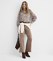 A woman in a patterned blouse and brown corduroy pants stands against a plain white background, holding a brown purse. carousel Product Image 3