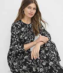 A woman in a black floral dress with long sleeves sits in front of a plain white background. carousel Product Image 1