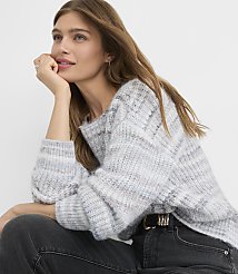 A woman in a grey and white patterned sweater and dark jeans rests her chin on her hand against a plain white background. carousel Product Image 1