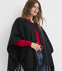 A woman in a black fringed poncho over a red top and blue jeans stands against a plain white background. carousel Product Image 2