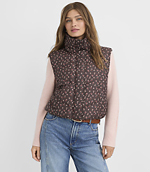 A woman in a floral puffer vest and pink sweater stands against a plain background. carousel Product Image 1