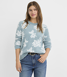 A woman in a fuzzy blue sweater with a floral pattern and jeans stands against a plain, light background. carousel Product Image 2