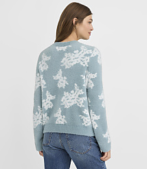 A woman in a fuzzy blue sweater with a white floral pattern stands against a plain, light blue background. carousel Product Image 3