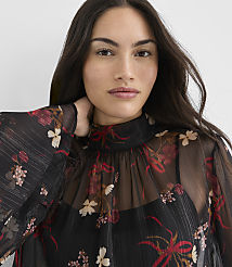 A woman with dark hair and a floral sheer top stands against a plain white background. carousel Product Image 2