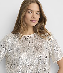 A woman with long, blonde hair wears a sparkling sequined top in the foreground, against a plain white background. carousel Product Image 2