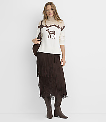 A woman in a cream sweater with a deer motif and a brown fringed skirt stands against a plain white background. carousel Product Image 3