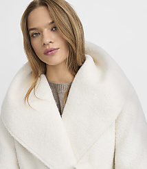 A woman with blonde hair and a neutral expression wears a cream-colored coat with a large collar, set against a plain white background. carousel Product Image 4