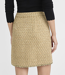 A woman in a black scalloped-hem top models a textured beige tweed mini skirt with a fringed hem against a plain gray background. carousel Product Image 3