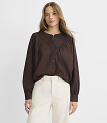 A woman in a brown blouse and cream pants stands against a plain white background. carousel Product Image 1