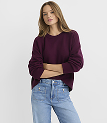 A young woman in a plum-colored sweater and embellished jeans stands with her arms crossed against a plain white background. carousel Product Image 1