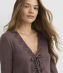 A woman with long, brown hair wears a brown, lace-trimmed V-neck top against a plain, light gray background. carousel Product Image 4