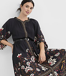 A woman in a black floral dress with a cinched waist stands against a plain white background. carousel Product Image 1
