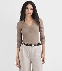 A woman in a brown lace-trimmed top and light-colored pants stands against a plain white background. carousel Product Image 1