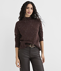 A woman in a speckled brown turtleneck sweater and dark pants stands against a plain gray background. carousel Product Image 2