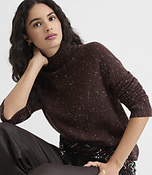 A woman in a speckled brown turtleneck sweater rests her arm on her knee against a plain white background. carousel Product Image 3
