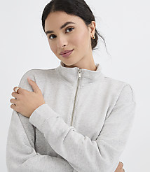 A young woman with dark hair and a light grey zip-up sweatshirt is posed against a plain white background. carousel Product Image 1