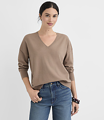 A woman in a brown v-neck sweater and blue jeans stands against a plain white background. carousel Product Image 1