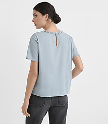 A woman in a light blue top and dark jeans stands against a plain white background. carousel Product Image 3