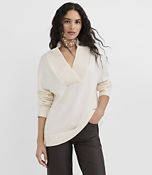 A woman in a cream-colored sweater and dark pants stands against a plain gray background. carousel Product Image 1