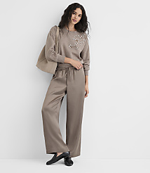 A woman in a taupe sweatshirt with pearl embellishments and matching satin pants stands against a plain white background, carrying a large tote bag. carousel Product Image 3