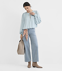A woman in a light blue blouse and wide-leg pants stands against a plain white background, holding a tan tote bag. carousel Product Image 2