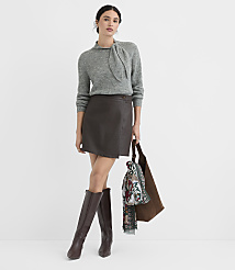 A woman in a grey sweater, brown leather skirt, and knee-high boots stands against a plain white background, holding a brown tote bag with a scarf draped over it. carousel Product Image 1