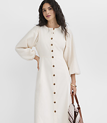 A woman in a cream-colored button-down dress with voluminous sleeves stands against a plain white background, holding a brown leather tote bag. carousel Product Image 2