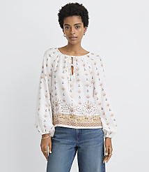 A woman in a patterned white blouse and blue jeans stands against a plain white background. carousel Product Image 1