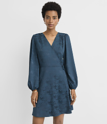 A woman in a teal wrap dress with a floral pattern stands against a plain gray background. carousel Product Image 1