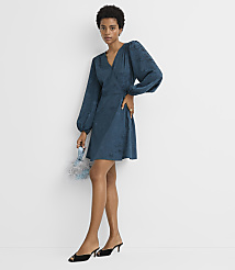 A woman in a teal wrap dress and black heels stands against a plain white background, holding a small blue beaded clutch. carousel Product Image 2