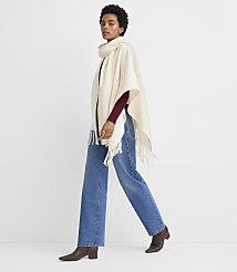 A woman in a cream-colored poncho and jeans walks against a plain white background. carousel Product Image 2