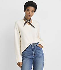 A woman in a cream v-neck sweater and blue jeans stands against a plain white background. carousel Product Image 1