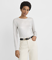 A woman in a shimmering silver long-sleeved shirt and cream pants with a black belt stands against a plain white background. carousel Product Image 1