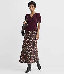 A woman in a burgundy velvet top and floral skirt stands against a plain white background. carousel Product Image 1