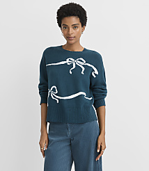 A woman in a teal sweater with white ribbon designs stands against a plain gray background. carousel Product Image 2