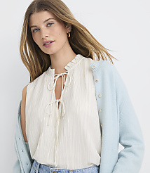 A woman in a cream-colored ruffled blouse and a light blue cardigan is shown against a plain white background. carousel Product Image 1