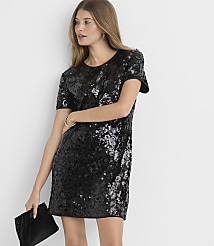 A woman in a sparkling black sequined dress and holding a black clutch stands against a plain white background. carousel Product Image 2