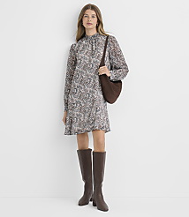 A woman in a patterned dress and brown boots stands against a plain white background, carrying a brown bag. carousel Product Image 1