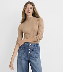 A woman in a tan ribbed mock-neck sweater and high-waisted blue jeans stands against a plain white background. carousel Product Image 1