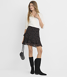 A woman in a floral skirt and white blouse stands against a plain white background, holding a black purse and wearing black boots. carousel Product Image 1