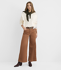 A woman in a cream cable-knit sweater, olive green scarf, and brown corduroy pants stands against a plain white background. carousel Product Image 1