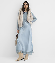 A woman in a light blue satin slip dress and a fuzzy vest stands against a plain white background. carousel Product Image 1