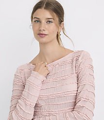 A young woman with blonde hair pulled back wears a textured pink top, with a plain white background. carousel Product Image 1