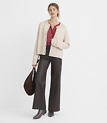 A woman in a cream cardigan and dark pants stands against a plain white background, holding a brown purse. carousel Product Image 2